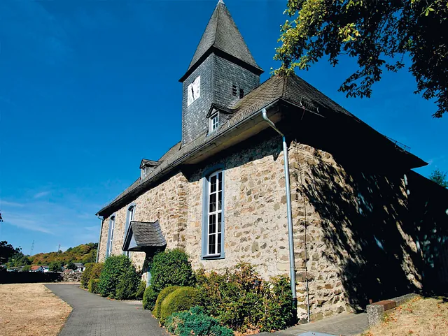 Historische Steinkirche mit spitzem Turm an einem gepflasterten Weg.