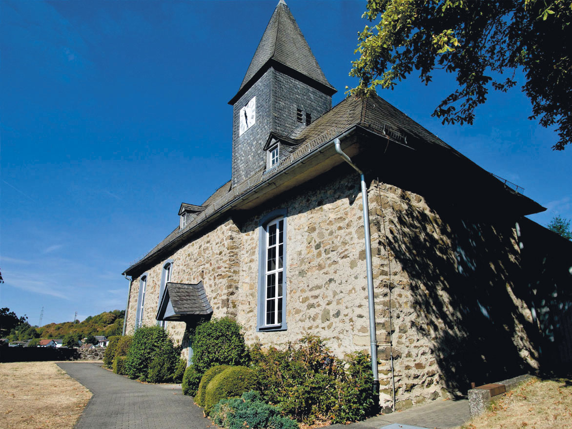 Historische Steinkirche mit spitzem Turm an einem gepflasterten Weg.