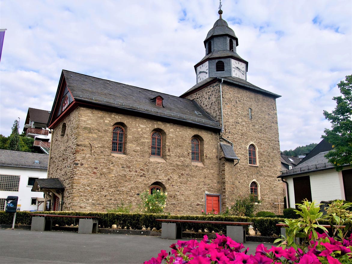 Ansicht einer historischen Steinkirche mit Blumenbeeten im Vordergrund.