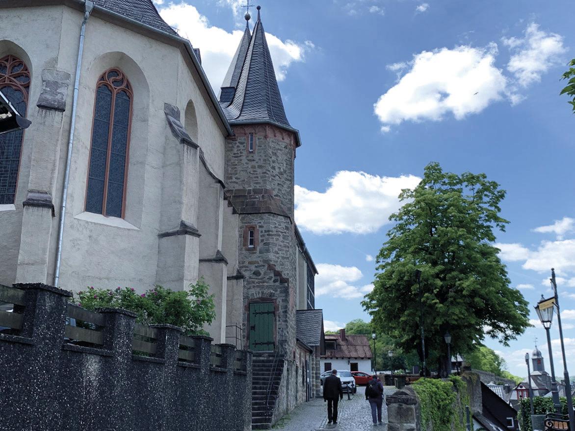 Seitenansicht einer alten Kirche an einer gepflasterten Straße mit Bäumen.