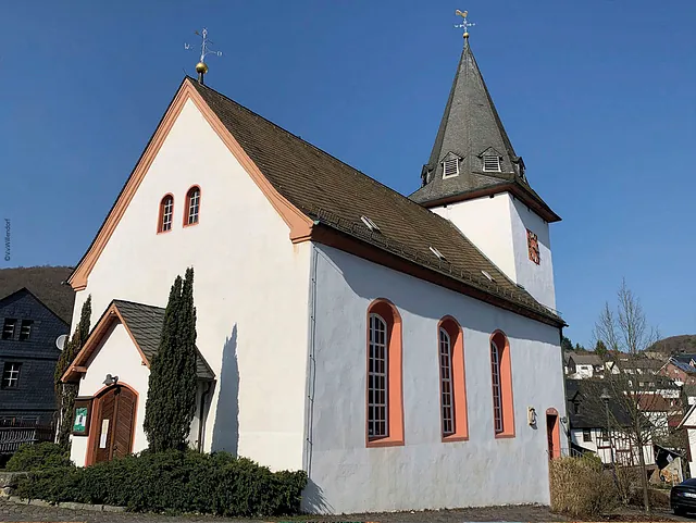 Außenansicht einer weißen Kirche mit spitzem Kirchturm unter blauem Himmel.