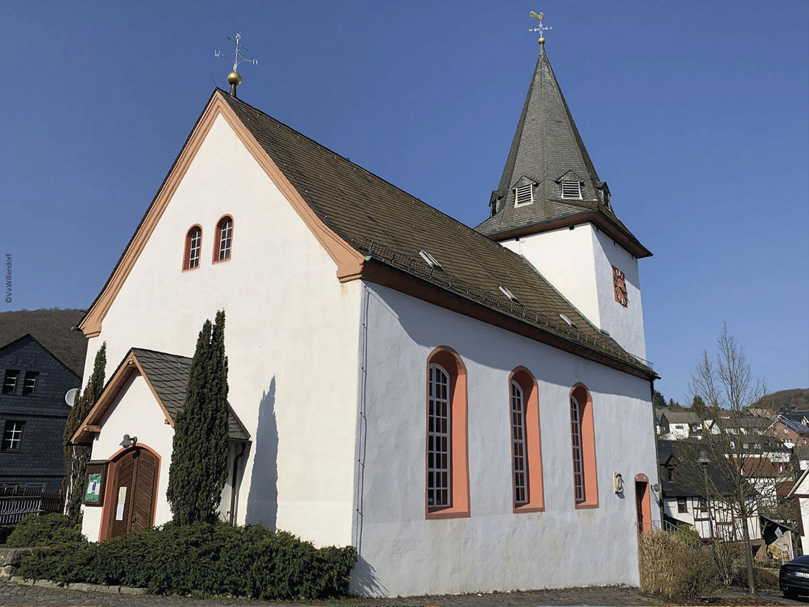 Außenansicht einer weißen Kirche mit spitzem Kirchturm unter blauem Himmel.